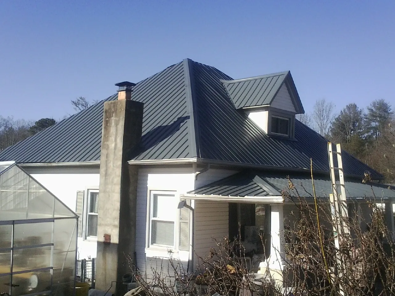 Dark blue standing seam metal roof on a white farmhouse with dormer — Slate & Tile Roof Repair by Roofing Brothers in Rockwell City