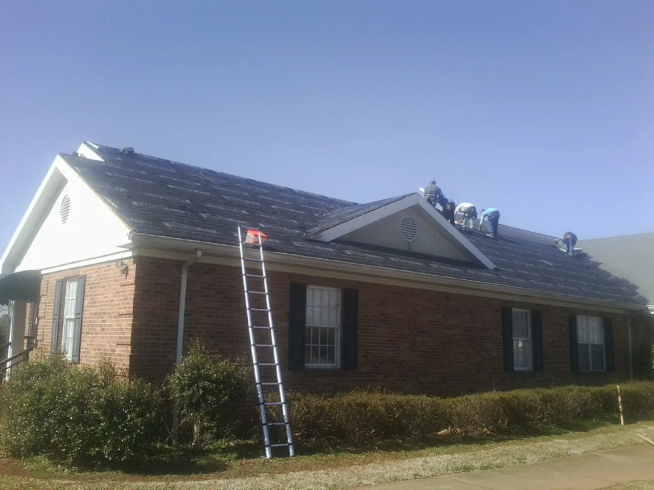 Crew tearing shingles off a brick ranch roof with a ladder set — Metal Roof Repair work by our crew in Rockwell City
