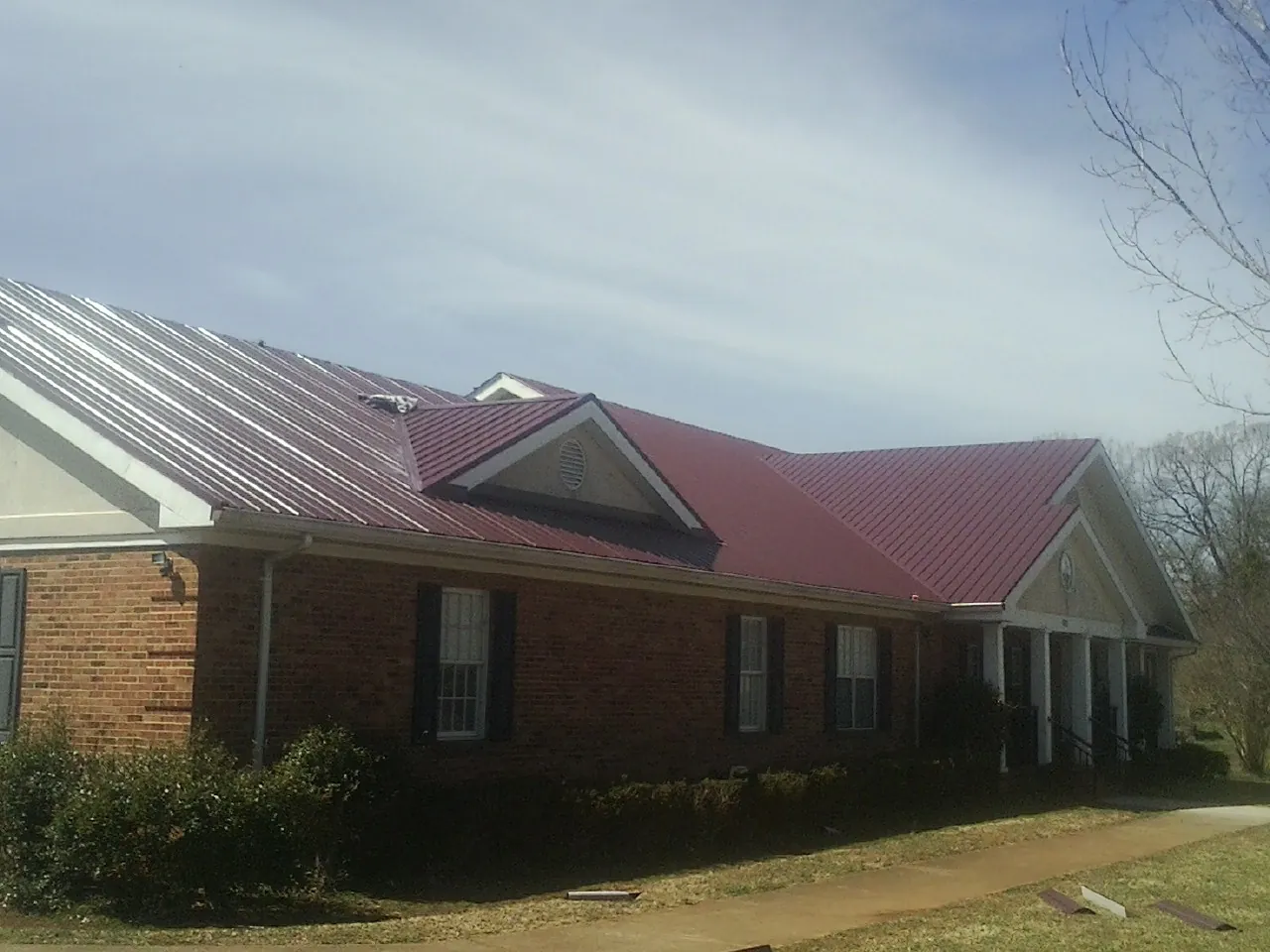 Red metal roof with gabled entries on a long brick building, from a Hail Damage Roof Repair job in Rockwell City
