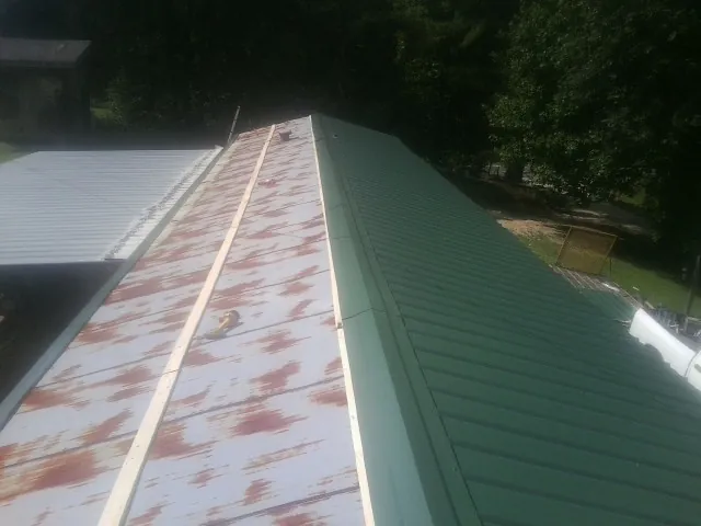 Old rusted panels beside newly installed green metal roofing — Wind Damage Roof Repair by Roofing Brothers in Rockwell City