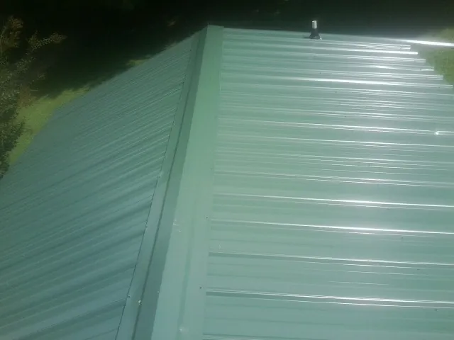 New green metal panels meeting at the ridge of a roof — Flat Roof Repair work by our crew in Rockwell City