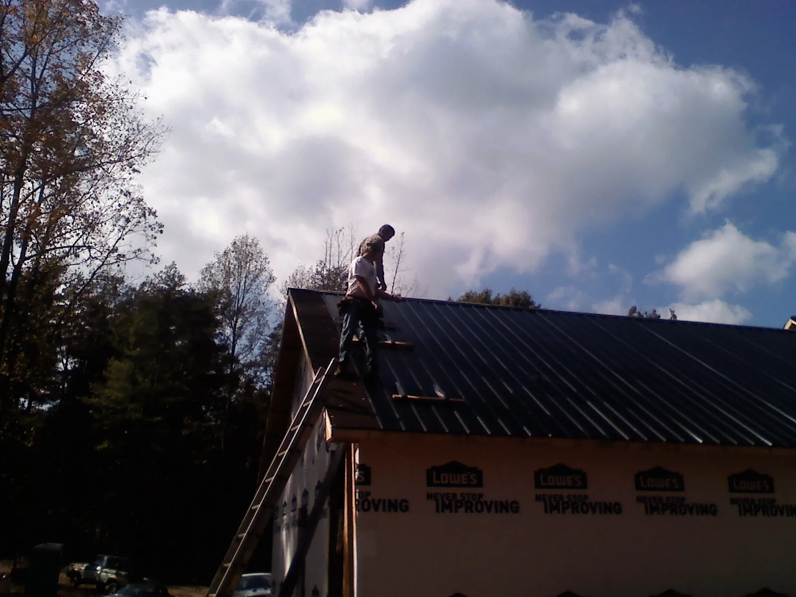 Roofer fastening dark metal panels high against a cloudy sky, from a Roof Inspection job in Rockwell City