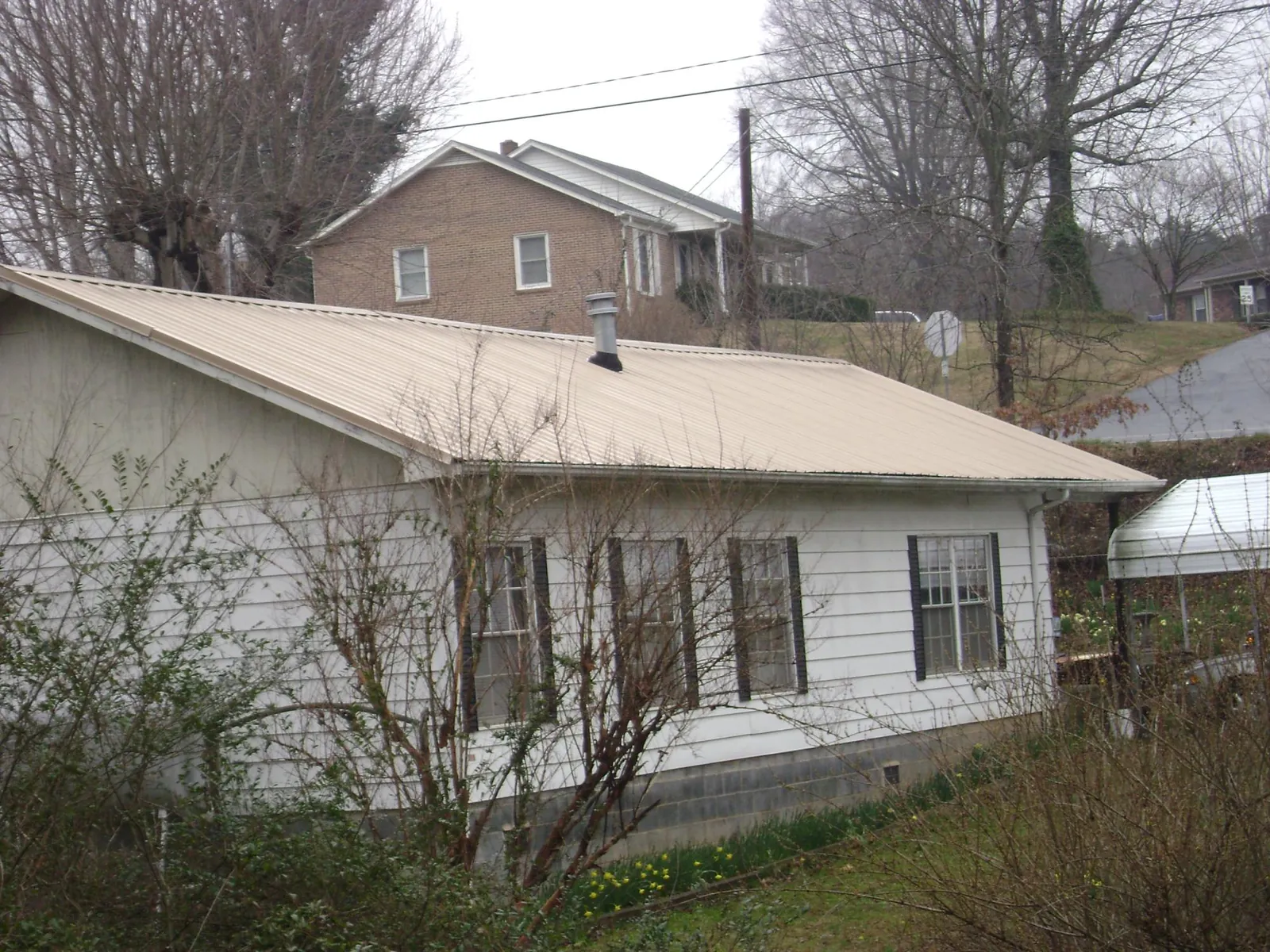 Tan metal roof on a white sided house set into a hillside — Commercial Roofing by Roofing Brothers in Rockwell City